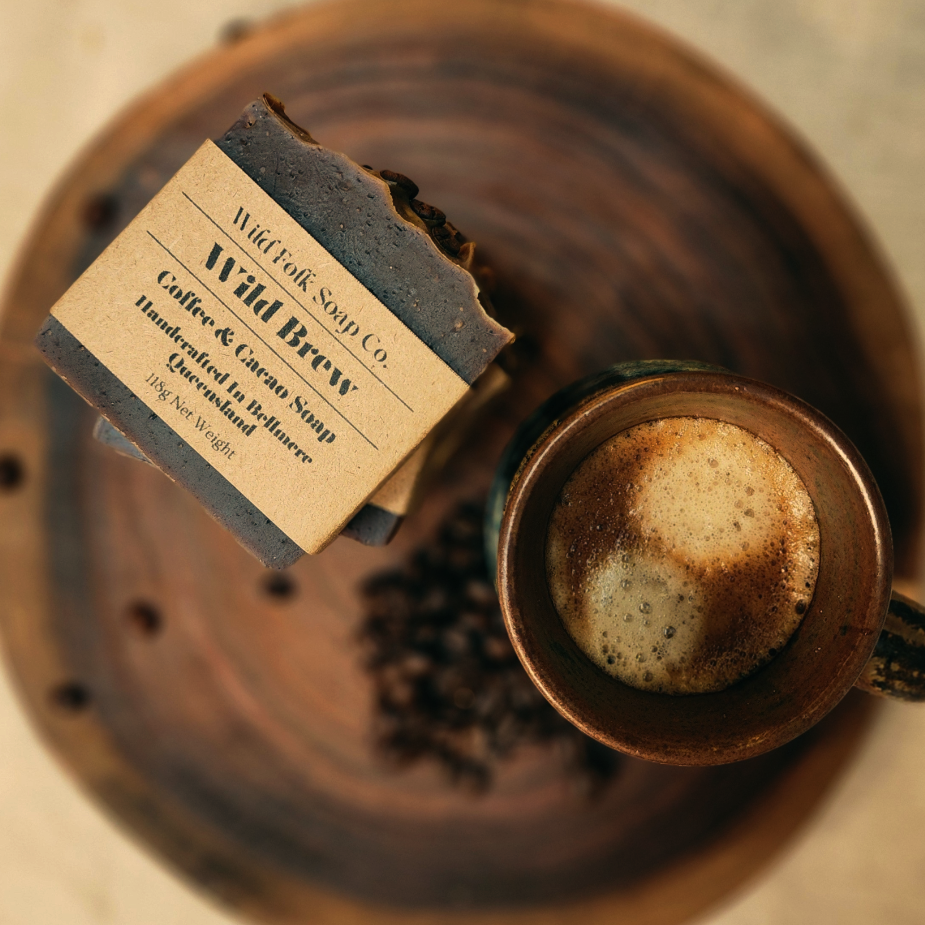 Wild Brew cold process coffee soap from Wild Folk Soap Co. on a wooden surface with coffee beans and a cup of coffee.