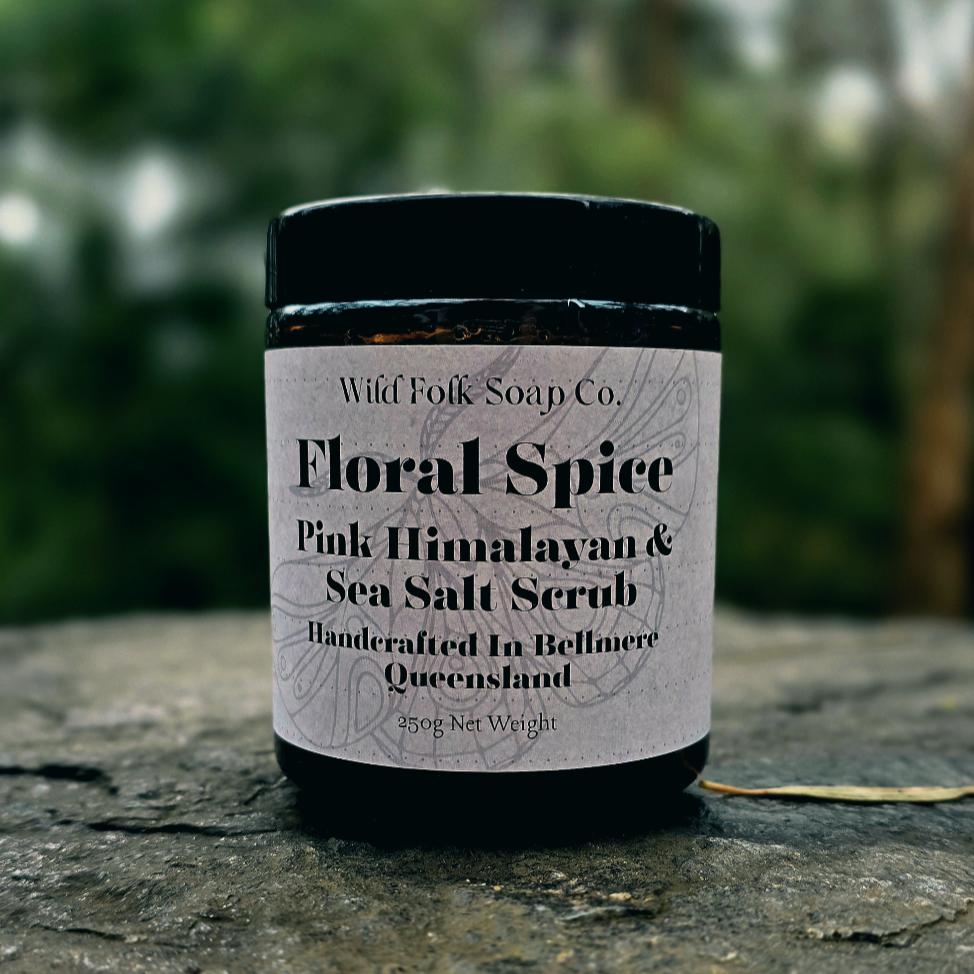 Jar of Wild Folk Soap Co. Floral Spice Pink Himalayan & Sea Salt Scrub on a stone surface with a blurred green background.