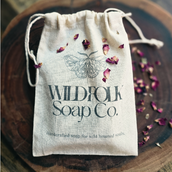 Drawstring bag with 'Wildfolk Soap Co.' branding on a wooden surface with dried flowers.