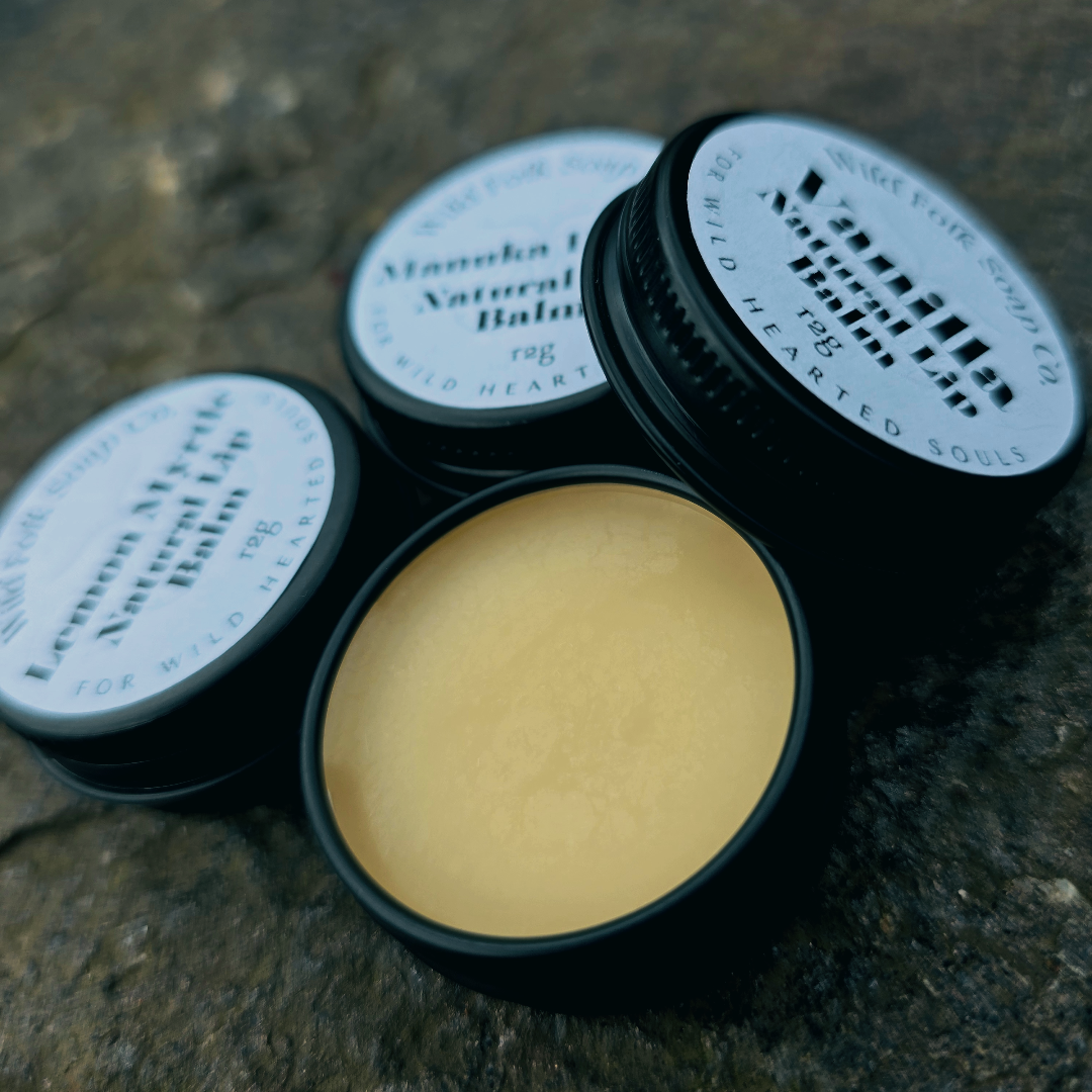 Three tins of lip balm with white labels on a textured surface