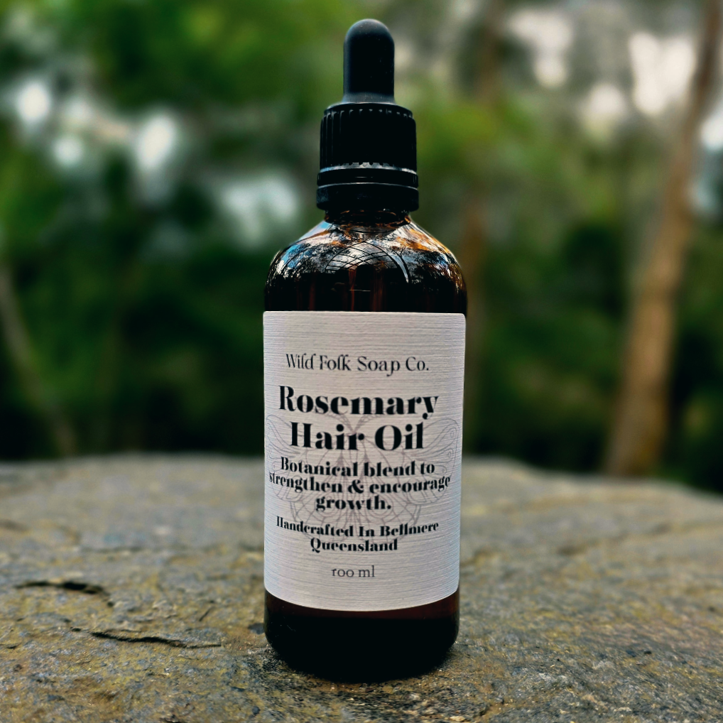 Bottle of Wild Folk Soap Co. Rosemary Hair Oil on a rock with a blurred natural background