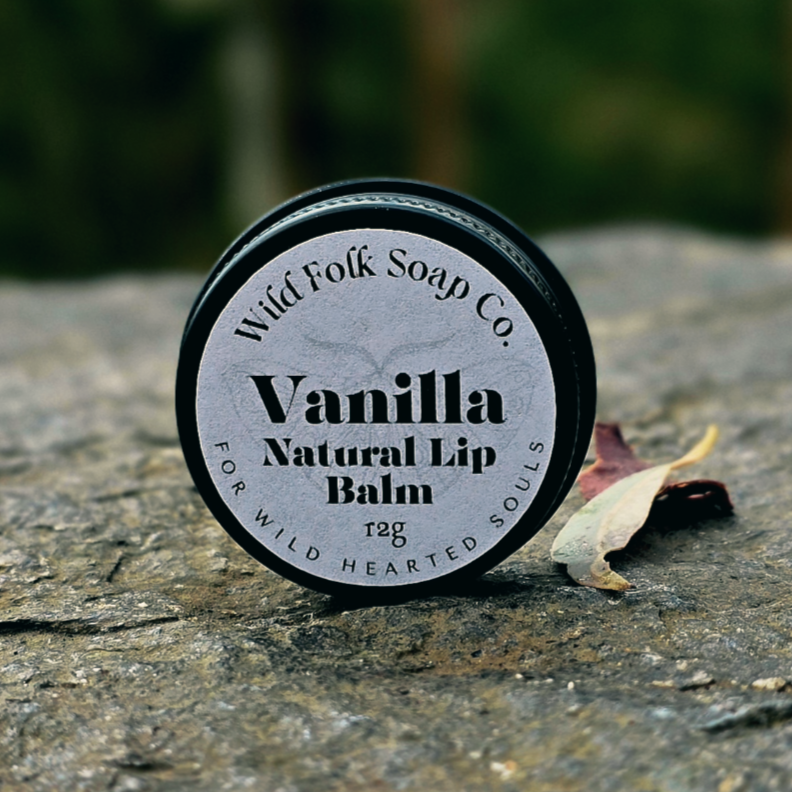 Vanilla natural lip balm container on a stone surface with blurred greenery in the background