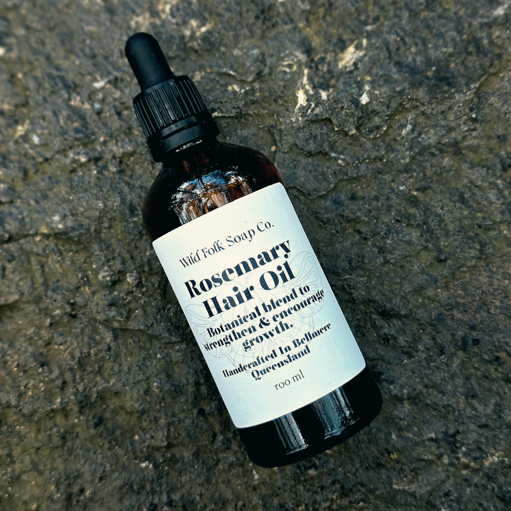 Rosemary hair oil bottle with dropper on a textured surface