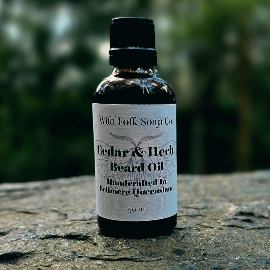 Bottle of Cedar & Herb Beard Oil by Wild Folk Soap Co. on a stone surface with a blurred natural background.