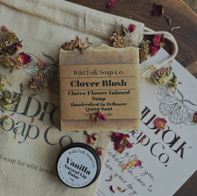 Bar of soap with packaging and a lip balm on a surface with 'Wild Folk Soap Co.' branding.