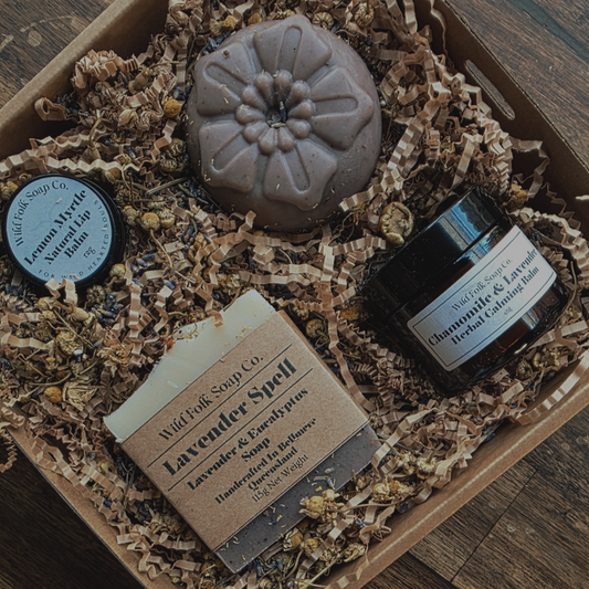 Set of natural skincare products including a bar of soap, cream, and bath bomb on a wooden surface.