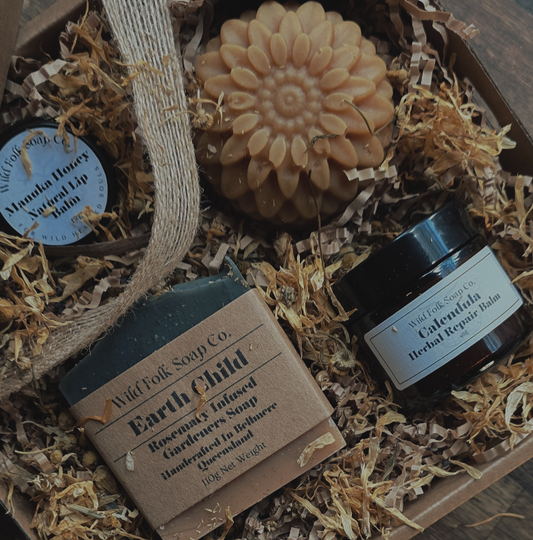 Box with natural skincare products including a bar of soap, lip balm, and cream on a wooden surface.